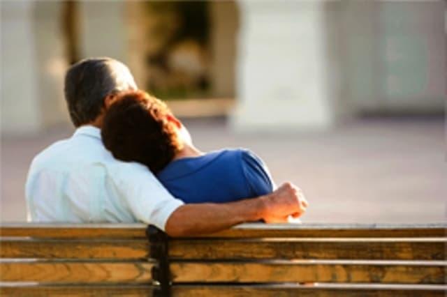 A couple sitting on a park bench with one partner resting their head on the other’s shoulder, capturing a peaceful moment of love, comfort, and companionship outdoors.