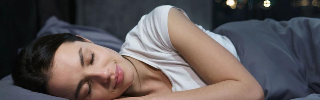 Person sleeping peacefully on their side in a dark, quiet bedroom, representing how to sleep better and improve rest and overall well-being.