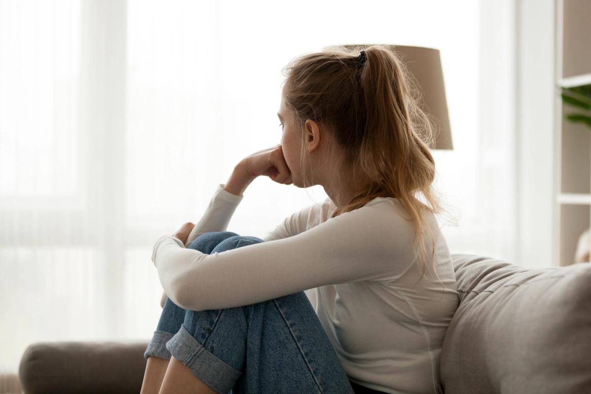 A woman sitting alone, looking distressed, illustrating how women face unique challenges from alcohol addiction, including emotional isolation and stigma.