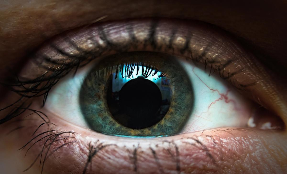 Extreme close up of a human eye showing detailed iris texture, dark pupil, visible eyelashes, and subtle red veins in the white of the eye, highlighting vision, perception, and eye health.