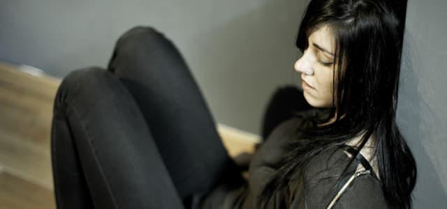 A woman wearing all black, sitting on the ground looking distraught.